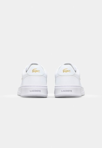 Бели кожени маратонки с плоска подметка, с златно лого на Lacoste и акценти на петата, с гладка текстура и минималистичен дизайн.