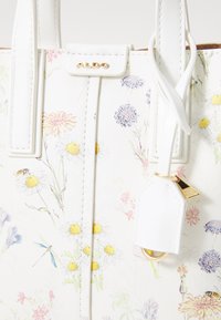 Blumige Tragetasche aus weißem synthetischen Material; zeigt farbenfrohe Blumenmuster und ein Logo in Goldton. Enthält ein abnehmbares Charm-Anhänger.
