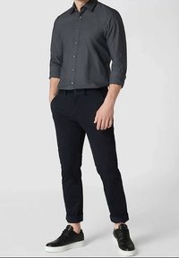 Tmavosivá košeľa na zapínanie na gombíky, čierne zúžené nohavice a čierne tenisky s bielou podrážkou. Košeľa má zavinuté rukávy a klasický golier.