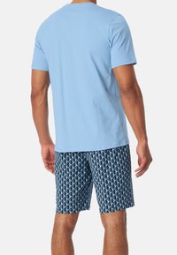Světle modré tričko s krátkým rukávem v kombinaci s vzorovanými námořnickými plavkami, které mají geometrický design v světle modrých tónech.