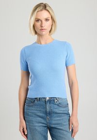 Short-sleeve, ribbed light blue sweater with a round neckline, fitted design, and soft texture, paired with high-waisted denim jeans.