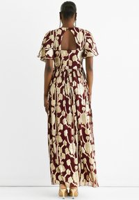 Maxi dress with burgundy fabric featuring gold floral pattern, flutter sleeves, and a keyhole back design. Smooth texture and flowing silhouette.
