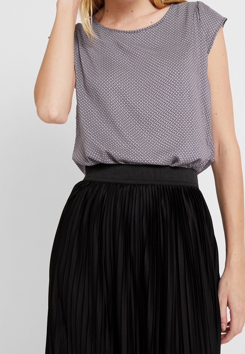 Svart plisserad kjol med elastisk midja som parkeras med en ljusgrå topp med kort ärm, prydd med ett geometriskt mönster och texturerad material.