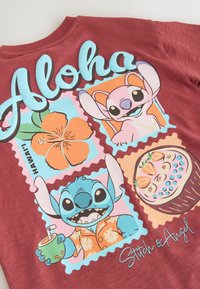 Chemise rouge avec le texte "Aloha", les personnages de dessin animé Stitch et Angel, une fleur d'hibiscus et un bol de fruits contenant des fraises et des myrtilles.