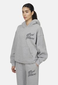 Felpa grigia in cotone misto, con tasca frontale e testo "Good for Nothing" in grigio scuro. Abbinata a pantaloni della tuta coordinati.