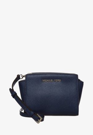 Granatowa skórzana torba na ramię o fakturowanej powierzchni, złote logo z przodu i odpinany pasek. Prostokątny kształt z kątowymi narożnikami.