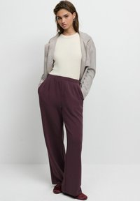Pantaloni bordo cu talie elastică și croială lejeră, asortați cu un top bej deschis și o jachetă gri cu fermoar. Textură netedă, design cu picior larg.