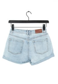 Shorts de mezclilla en azul claro con dobladillo deshilachado, que cuentan con una etiqueta de cuero marrón en la parte posterior de la cinturilla y dos bolsillos traseros.