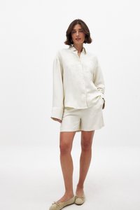 Crème kleurige linnen overhemd met een knoopsluiting en lange mouwen, gecombineerd met bijpassende shorts, beide met een ontspannen pasvorm en een gladde textuur.