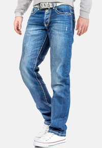 Blauwe denim jeans met een rechte pijp, vervaagd einde, witte stiksels en een vijf-pocket ontwerp, gecombineerd met witte sneakers.