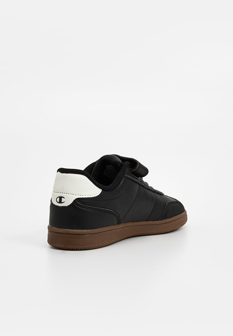 Baskets noires avec semelle marron, patch de talon blanc arborant un logo noir et bande Velcro, vues de l'arrière sur fond blanc.