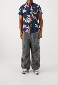 Short-sleeve navy shirt with pink floral pattern, paired with loose, light grey pants and silver athletic shoes.