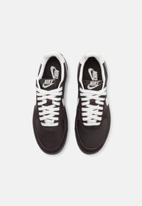 Crne tenisice s bijelim vezicama, izrađene od glatke kože i teksturirane suede gornje strane, okrugli vrh i istaknuti Nike logo na jeziku.