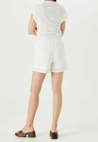 Biała bluzka z ażurowej tkaniny z krótkimi rękawami oraz pasujące białe szorty. Szorty mają elastyczną talię. Dopełnieniem stroju są brązowe sandały na obcasie.