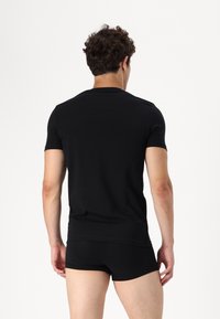 Svart t-skjorte med kort erm og svarte boxershorts, vist bakfra. Glatt stoff, tettsittende design, minimal detaljering. Enkelt ensfarget.