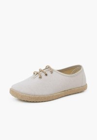 Scarpa in tela beige con punta arrotondata, design con lacci e suola in tessuto di juta. Presenta occhielli in metallo e una silhouette bassa.
