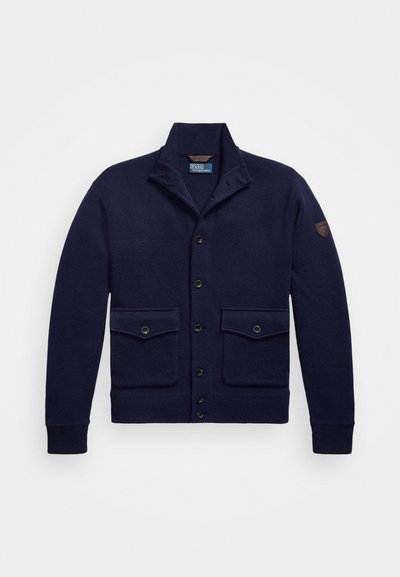 Tamnok modri kardigan iz pletene tkanine, ki ima šal ovratnik, gumbe spredaj, dve sprednji žepi in detajl na rami.