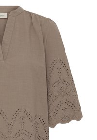 Blouse taupe avec encolure en V et manches 3/4, ornée d'une broderie ajourée complexe et de bords festonnés.