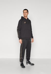 Zwart hoodie en sweatpants set met gouden logo-accenten en gestreepte zijstrips. Gemaakt van een gladde stof met een relaxte pasvorm.