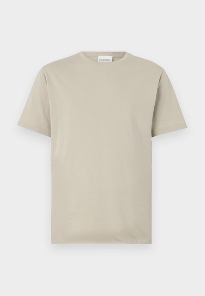 Camiseta de algodón color beige, de manga corta, con cuello redondo, en color sólido sin patrones, corte relajado, con una etiqueta que dice "CLOSED" en el cuello.
