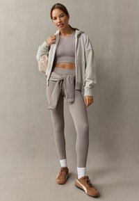 Svijetlo siva dukserica sa zipom, uskla�đeni crop top, i helanke visokog struka. Smeđe atletske cipele s bijelim čarapama. Meki, rastezljivi materijal.