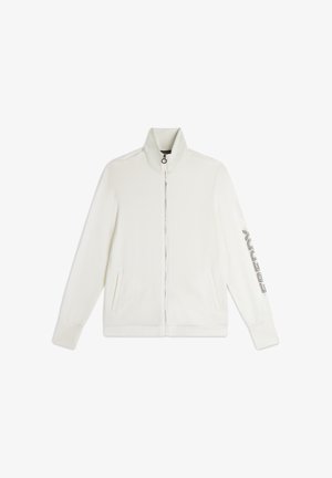 Chaqueta blanca con cremallera y cuello alto, dos bolsillos laterales y detalle de texto decorativo en la manga izquierda. Textura de tela suave.