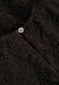 Gros plan sur un tissu jacquard noir à motif floral avec un petit bouton rond blanc unique près de la couture du col.
