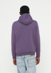 Sweat à capuche violet ample avec une grande capuche, fabriqué en tissu doux. Doté de poignets et d'une ceinture côtelés, accompagné d'un jean bleu clair.