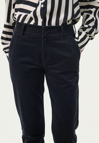 Dark navy corduroy trousers with a smooth texture, featuring side pockets and a fitted waistband, paired with a black and white striped blouse.