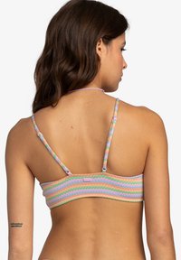 Bikiniöverdel med flerfärgade zigzag-mönster och tunna band, med en rosa märkeslapp på mitt bak. Tillverkad av mjukt, elastiskt tyg.