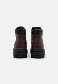 Botas de tobillo de cuero marrón con suelas de goma negra, cuellos acolchados y detalle del logo en relieve sobre el talón. Textura suave, diseño robusto.