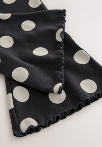 Sciarpa blu scuro con grandi pois bianchi, caratterizzata da un tessuto strutturato e bordi arricciati. Superficie liscia con una sensazione morbida.