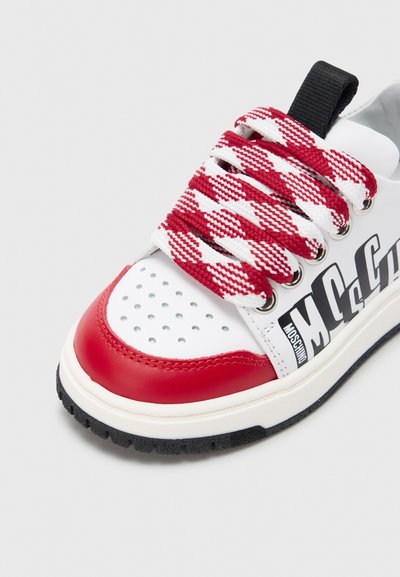 Λευκό αθλητικό παπούτσι με κόκκινες πινελιές, διαθέτει υφασμένα κορδόνια με κόκκινο και άσπρο καρό σχέδιο, διάτρητη περιοχή στα δάχτυλα και μαύρη ελαστική σόλα. Το λογότυπο εμφανίζεται στο πλάι.