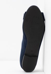 Chaussure en daim bleu marine avec une tige lisse, bout rond, petit talon et semelle en caoutchouc noir texturé marquée de la taille 37.