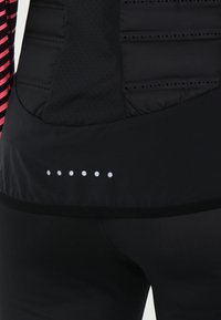 Černá sportovní bunda s texturovaným, polstrovaným zadním dílem, růžovými pruhovanými stranami a pěti malými bílými tečkami na dolním okraji.