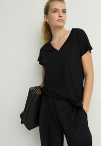 Zwarte v-hals t-shirt met korte mouwen, gemaakt van lichtgewicht stof. Gecombineerd met zwarte broek en een gestructureerde zwarte tas met stiksels.