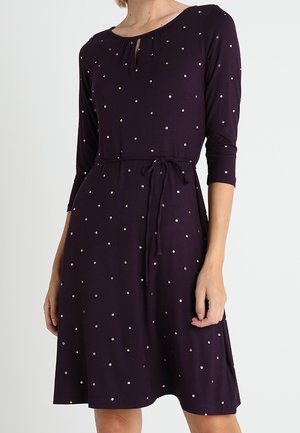 Tumma purppuranvärinen polvipituinen mekko, jossa on puolipitkät hihat, pienet valkoiset pilkut, pyöreä pääntie avauksella ja solmittava vyötärövyö.