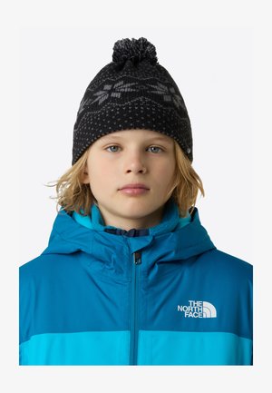 Geacă de iarnă albastră cu guler pufos și logo, purtată cu o căciulă neagră tricotată, având un pompon și modele geometrice.