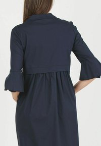 Abito blu navy con corpino aderente, maniche svasate e vita arricciata. Tessuto liscio con design semplice ed elegante.