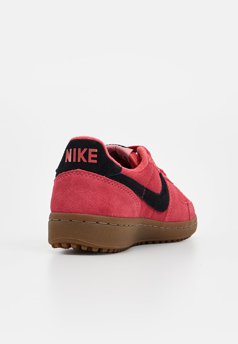 Zapatilla Nike de ante roja con acentos negros y suela de goma marrón. Presenta la marca "NIKE" en el talón y un interior acolchado.