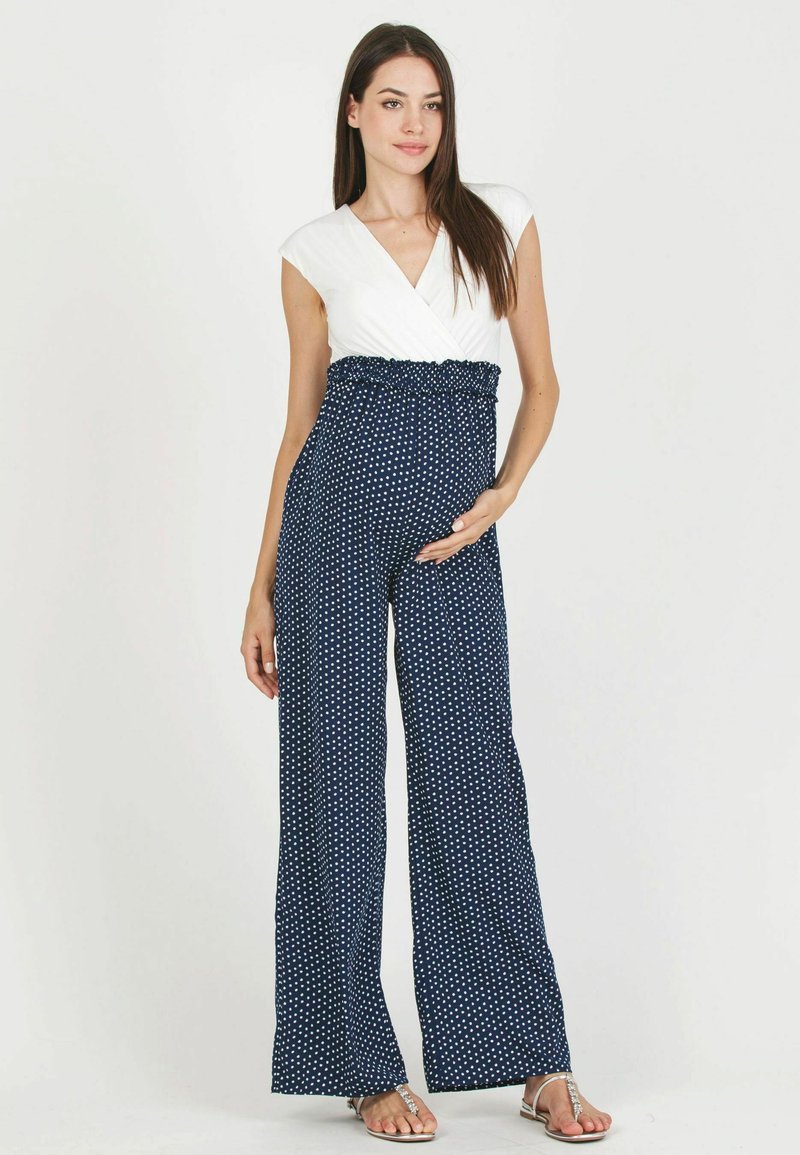 Combinaison bleu marine à pois avec un top croisé blanc et une taille froncée. Présente un design à jambes larges et une coupe décontractée. Tissu léger.