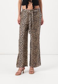 Leopardenmuster weite Hosen aus beige-braunem Stoff, mit einer Krawatte auf der Taille und glatter Textur. Kombiniert mit hautfarbenen Riemchenschuhen.