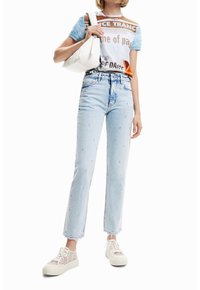 Ljusblå jeans med rak passform, prydda med pärlstickningar; kombinerade med en grafik-T-shirt och en vit handväska. Snygga sneakers fulländar looken.