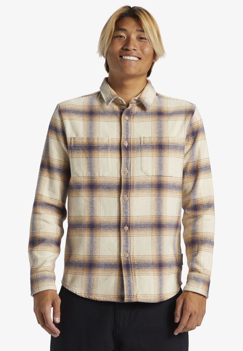 Camisa de franela con botones en un patrón de cuadros beige y púrpura, con cuello, mangas largas y un bolsillo en el pecho. Textura suave.