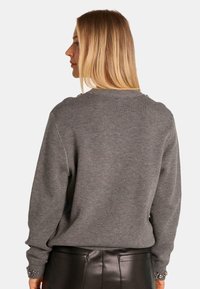 Grau gestrickter Pullover mit langen Ärmeln, Rundhalsausschnitt und strukturierten Akzenten an der Schulter. Kombiniert mit einem schwarzen Lederrock, der eine nahtlose Passform zeigt.