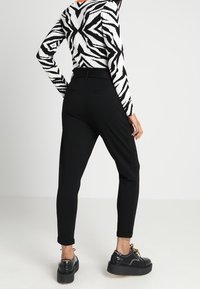 Zwarte slim fit broek met een gladde textuur, gecombineerd met een wit en zwart geblokt sweater met een zebra-patroon en stevige zwarte schoenen.