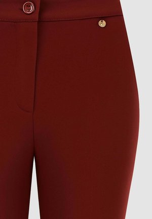 Pantaloni bordeaux con una texture liscia, chiusura frontale con bottoni e un dettaglio in oro. Progettati per una silhouette aderente.