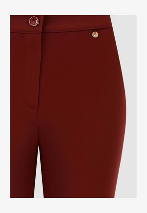 Pantaloni bordeaux con una texture liscia, chiusura frontale con bottoni e un dettaglio in oro. Progettati per una silhouette aderente.