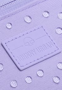 Tissu violet avec une surface texturée comportant des points clairs en relief et une étiquette en caoutchouc rectangulaire embossée avec "JOHNNY URBAN."