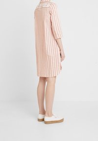 Vestido de rayas rosa claro con mangas tres cuartos y escote redondo, que presenta rayas verticales y un corte holgado, combinado con zapatos blancos.